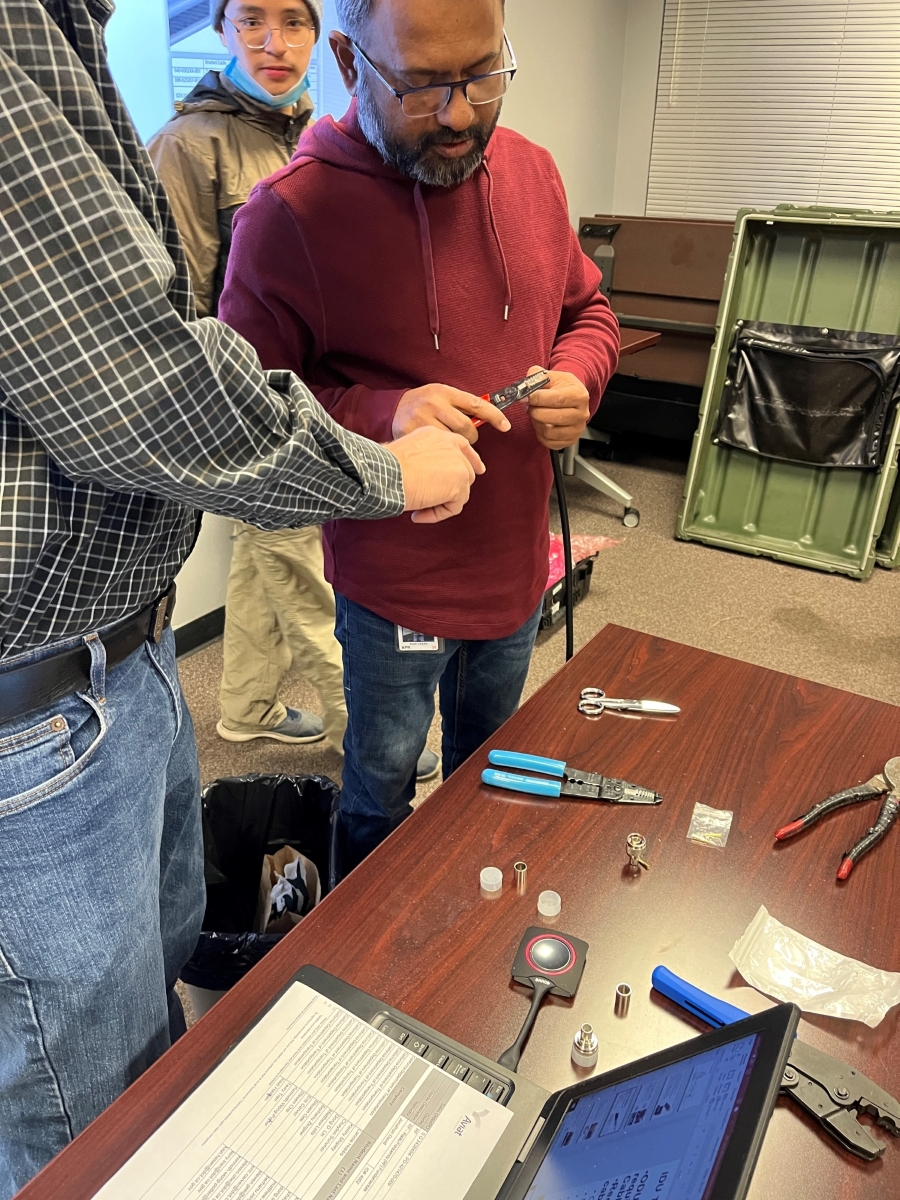 One of the students works on the cable and connector preparation lab exercise. A man holds a cable and a pair of pliers.